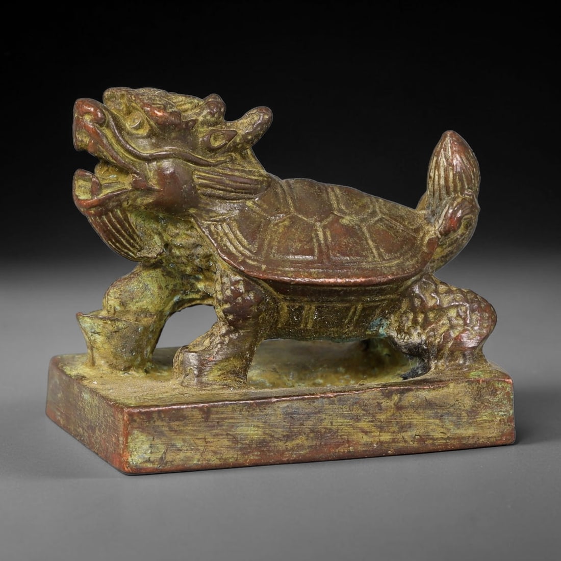 A Chinese Bronze Rectangular Seal with Dragon Turtle Knob, 22AX: Cast bronze rectangular seal topped with a detailed dragon turtle knob, modelled with an open-mouthed dragon head, segmented turtle shell and scaled limbs, perched upon the rectangular seal base. The 