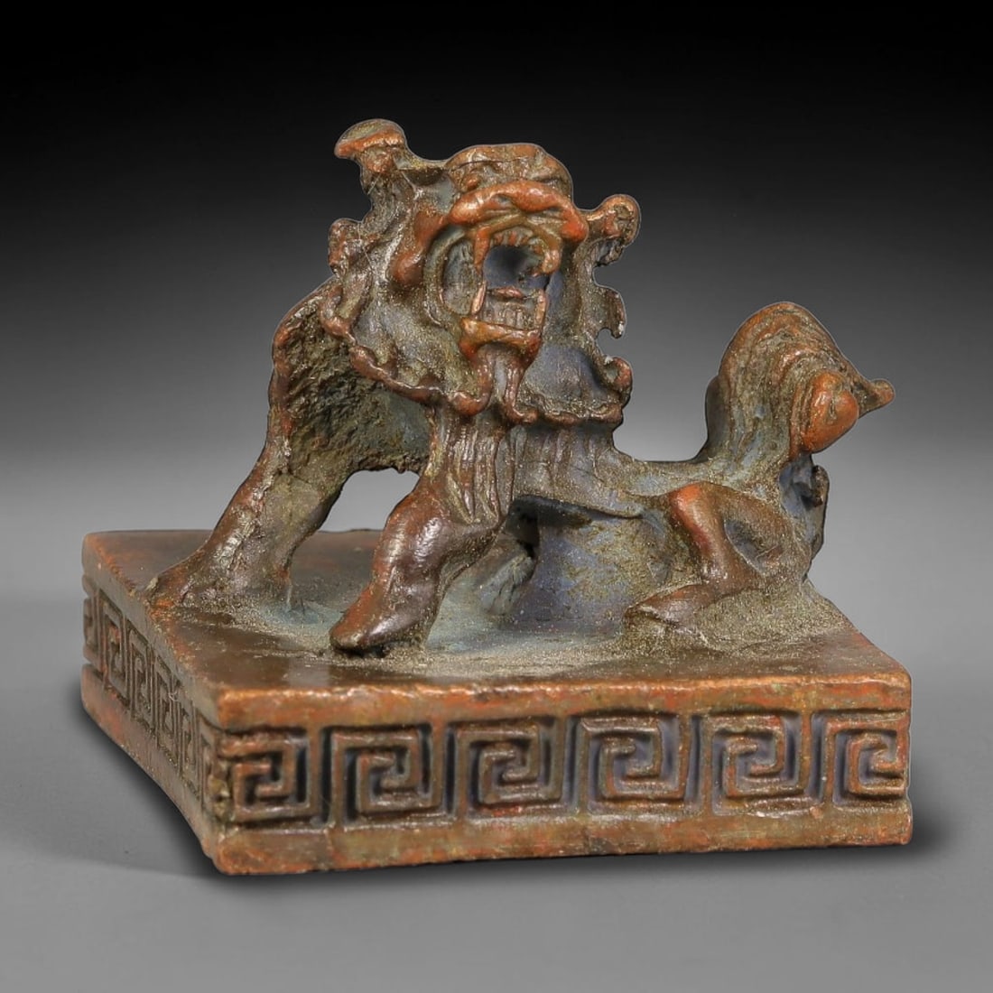 A Chinese Bronze Square Seal with Openwork Guardian Lion Knob, 26AX: Cast bronze square seal surmounted by a dynamically modelled openwork guardian lion knob with bared teeth and flowing mane details. The vertical sides of the seal block are decorated with continuous i
