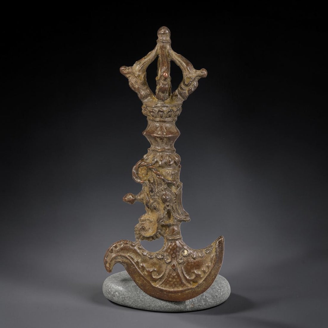 A Tibetan Bronze Kartika Axe with Vajra Finial, 68AX: Cast bronze kartika ritual axe topped with a five-pronged vajra finial, detailed with dragon head motifs at the base of the prongs. The central shaft is decorated with relief scrollwork and symbolic c