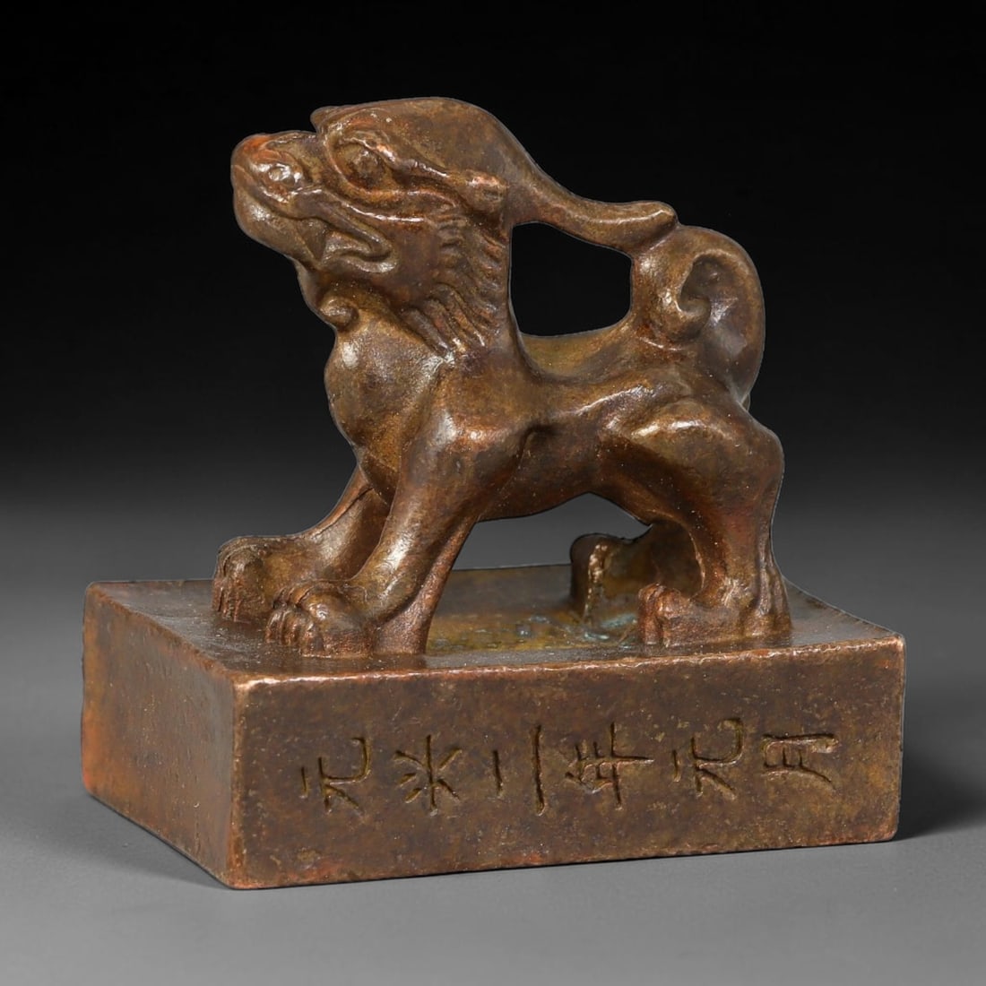 A Chinese Bronze Pixiu Stamp Seal, 21AX: Cast bronze rectangular seal surmounted by a standing Pixiu beast knob with defined facial features, curled tail and textured mane. The vertical side of the seal block bears an engraved dated inscript