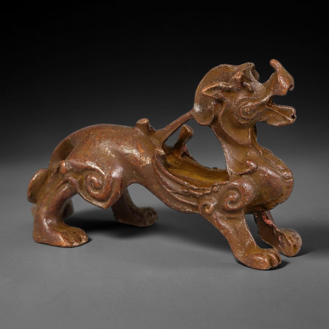 A Chinese Bronze Archaic Style Bixie Mythical Beast, 33AX: Cast bronze mythical bixie beast modelled in a striding posture with open mouth, stylized facial features, curled scroll ornamentation on the haunches and raised wing-like elements along its back. The