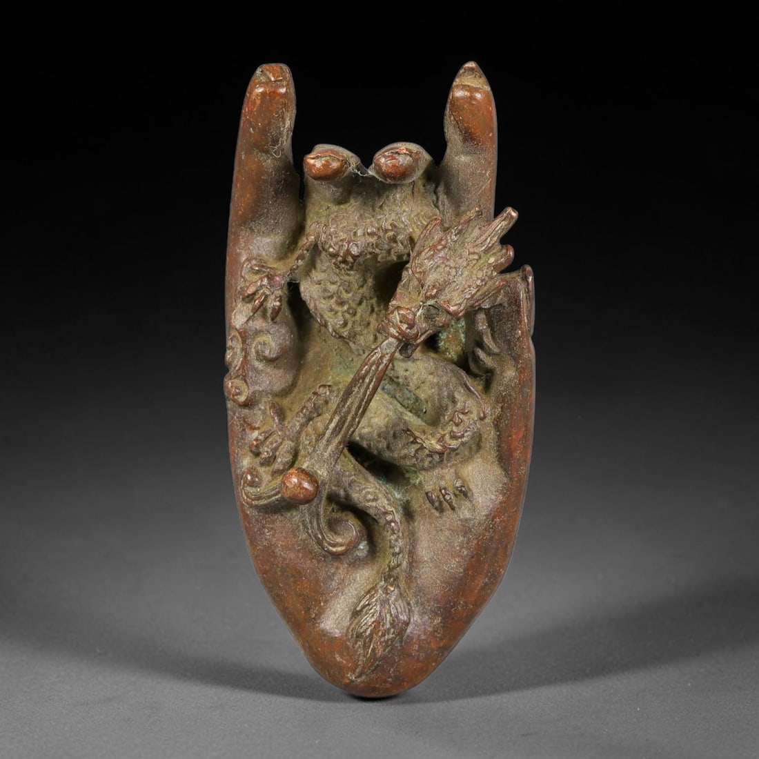 A Chinese Bronze Buddha Hand with Dragon Relief, 41AX: Cast bronze ornament modelled in the form of a Buddha hand with high relief coiled dragon grasping a pearl, fine scale and scroll detailing. The reverse bears an engraved Da Qing Qianlong mark. The br