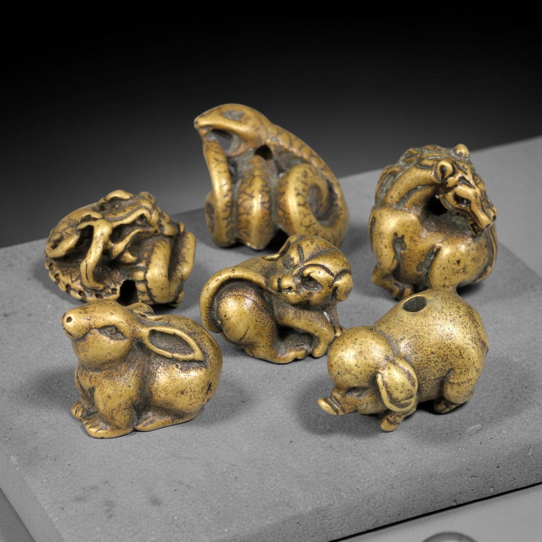 Lot of Six Chinese Bronze Zodiac Animal Beads, 74BD: Group of six cast bronze zodiac animal beads, each modelled as a distinct creature with a drilled hole for threading. The set includes rabbit, monkey, pig, horse, snake and dragon forms, rendered in c