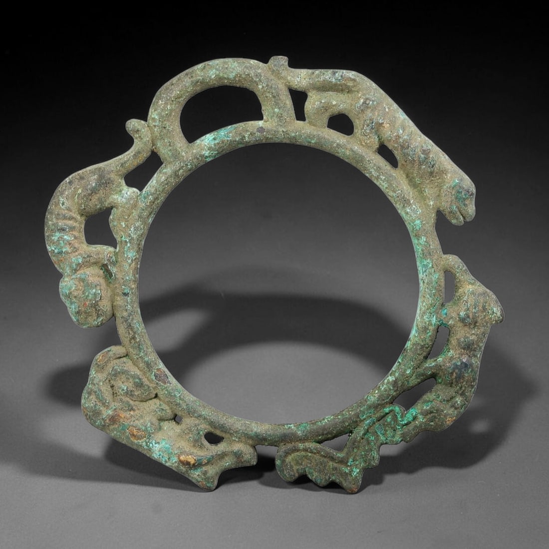 A Chinese Bronze Openwork Multi-Beast Amulet Ring, 56BD: Cast bronze openwork amulet ring adorned with multiple stylized beast figures integrated along the circular frame. The artifact bears heavy green burial patina and surface corrosion across the sculpte
