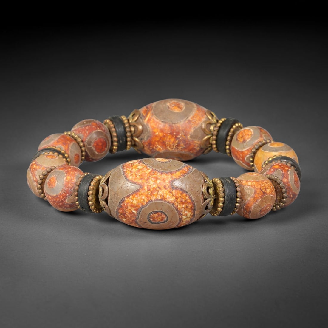 A Himalayan Tibetan Dzi Style Agate Bead Bracelet, 78BD: Bracelet assembled with large oval dzi style agate focal beads measuring 34.2 x 21.3mm paired with smaller matching patterned agate beads, separated by dark spacer discs and ornate brass filigree bead