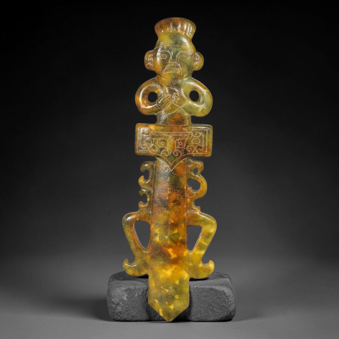 A Chinese Openwork Mottled Jade Anthropomorphic Dagger Pendant, 91AX: Vertically formed openwork jade pendant combining an archaic carved human figure at the top with a dagger-shaped blade below. The figure features incised facial details, a stylized headdress and loope