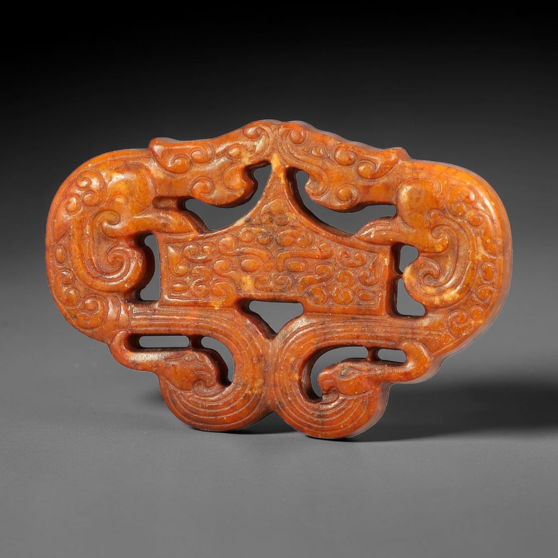 A Chinese Openwork Reddish-Brown Jade Dragon and Phoenix Pendant, 28BD: Openwork reddish-brown jade pendant with symmetrical composition. Two dragon heads are positioned at the upper terminals, paired with phoenix forms at the lower section. Fine incised scroll and linear