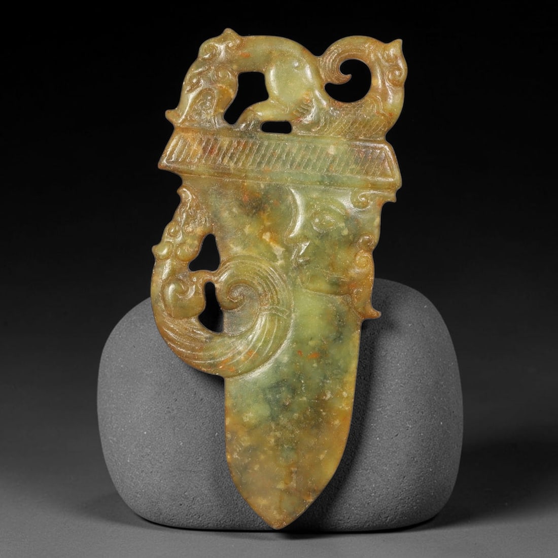 A Chinese Openwork Mottled Green Jade Ge Pendant with Beast Finial, 37BD: Dagger-axe (ge) form openwork jade pendant topped by a stylized curled beast figure with pierced negative space beneath its body. The rectangular guard is decorated with fine parallel incised linear o