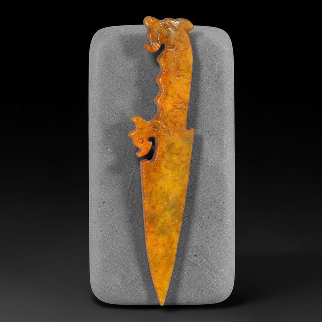 A Chinese Carved Golden Jade Dagger Pendant with Dragon Head Finial, 92AX: Slender dagger-shaped jade pendant topped by a detailed dragon head finial. The blade edge features stylized serrated ornamentation with a small openwork scroll cutout on one side. Fine incised detail