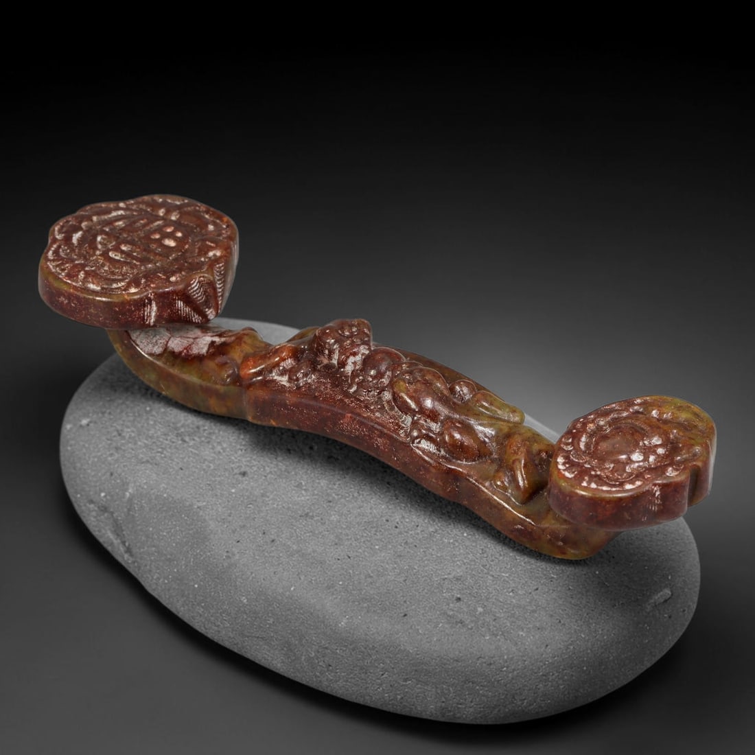 A Chinese Carved Mottled Russet and Green Jade Ruyi Scepter, 96AX: Small carved jade ruyi scepter featuring relief carved chilong ornamentation along the curved shaft. Both ruyi heads bear detailed auspicious motif carving. The stone has mottled deep reddish-brown an