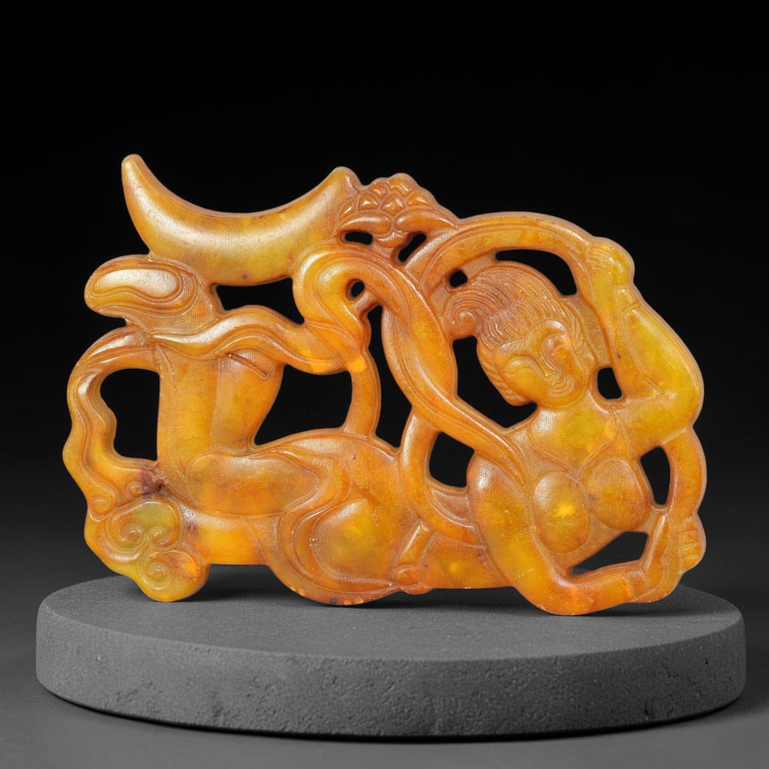 A Chinese Openwork Golden Jade Flying Apsaras Pendant, 2BD: Openwork golden jade pendant depicting a flying apsaras figure in flowing, dynamic pose. Stylized swirling ribbons interweave through negative cut-out spaces, paired with a crescent moon and floral or
