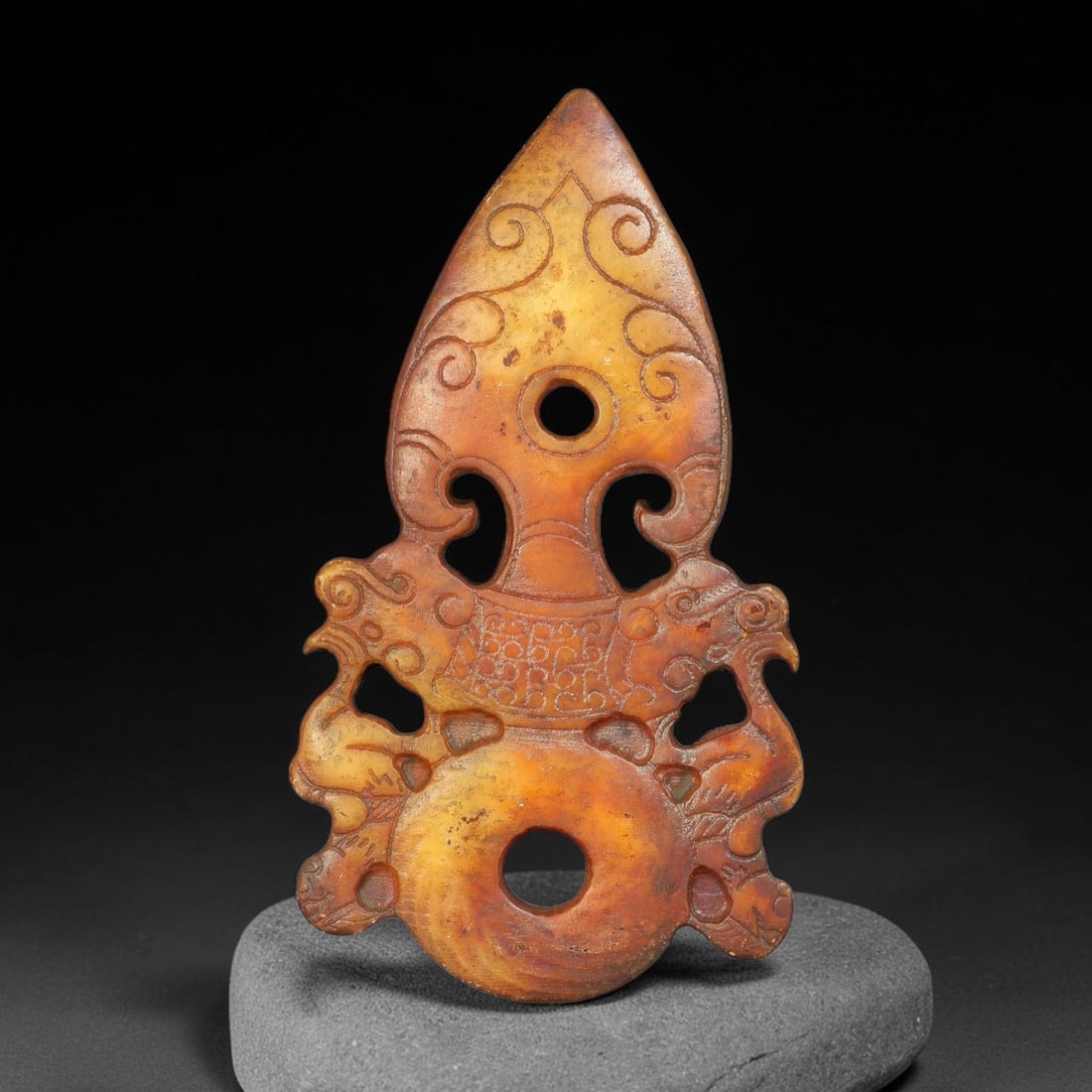 A Chinese Openwork Reddish Jade Spearhead Pendant with Twin Phoenix Motifs, 98AX: Openwork jade pendant constructed with an upper spearhead form decorated with incised scroll patterns and a central circular aperture. Symmetrical phoenix figures flank the midsection, their bodies de