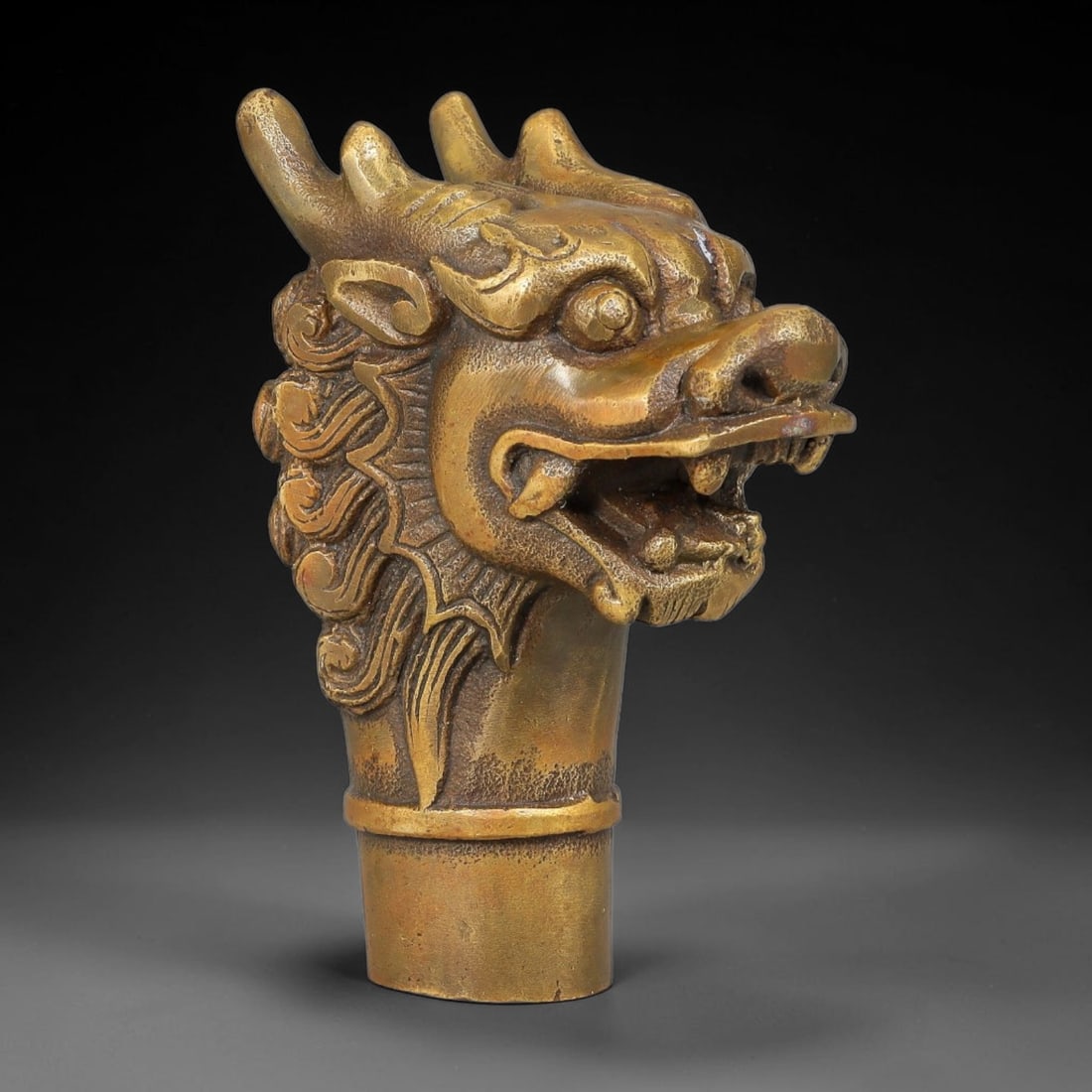 A Chinese Bronze Dragon Head Cane Handle, 70AX: Cast bronze cane handle modelled as a detailed dragon head with raised horns, defined eyes, open mouth and flowing relief mane ornamentation. The lower cylindrical socket is designed for mounting onto