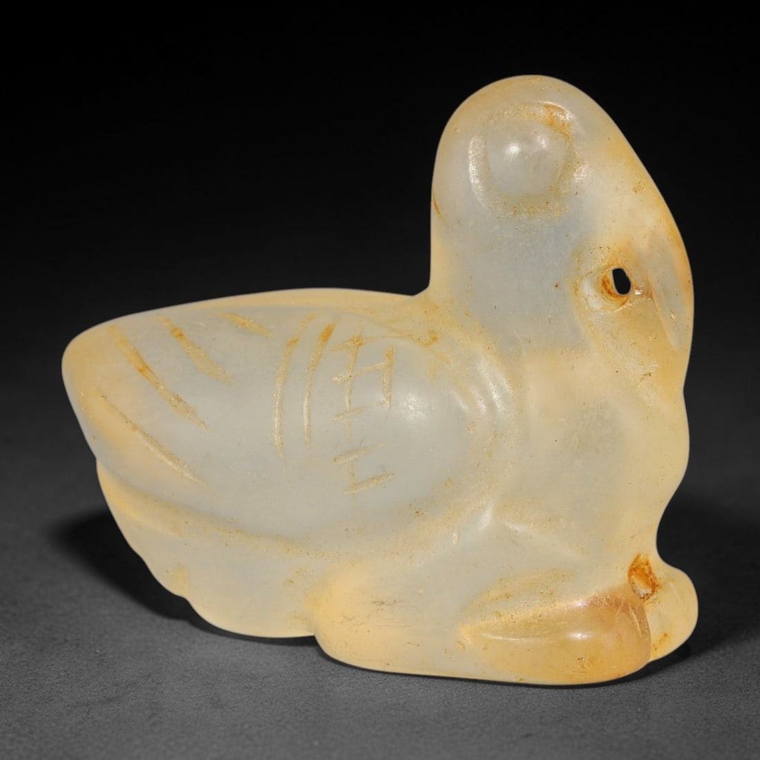A Chinese Archaistic Glass Recumbent Bird Carving, 9BF: Solid translucent glass carving of a recumbent bird with a long pointed beak, incised linear details decorating the body and wing sections. A perforation pierces the side of the head for suspension. T