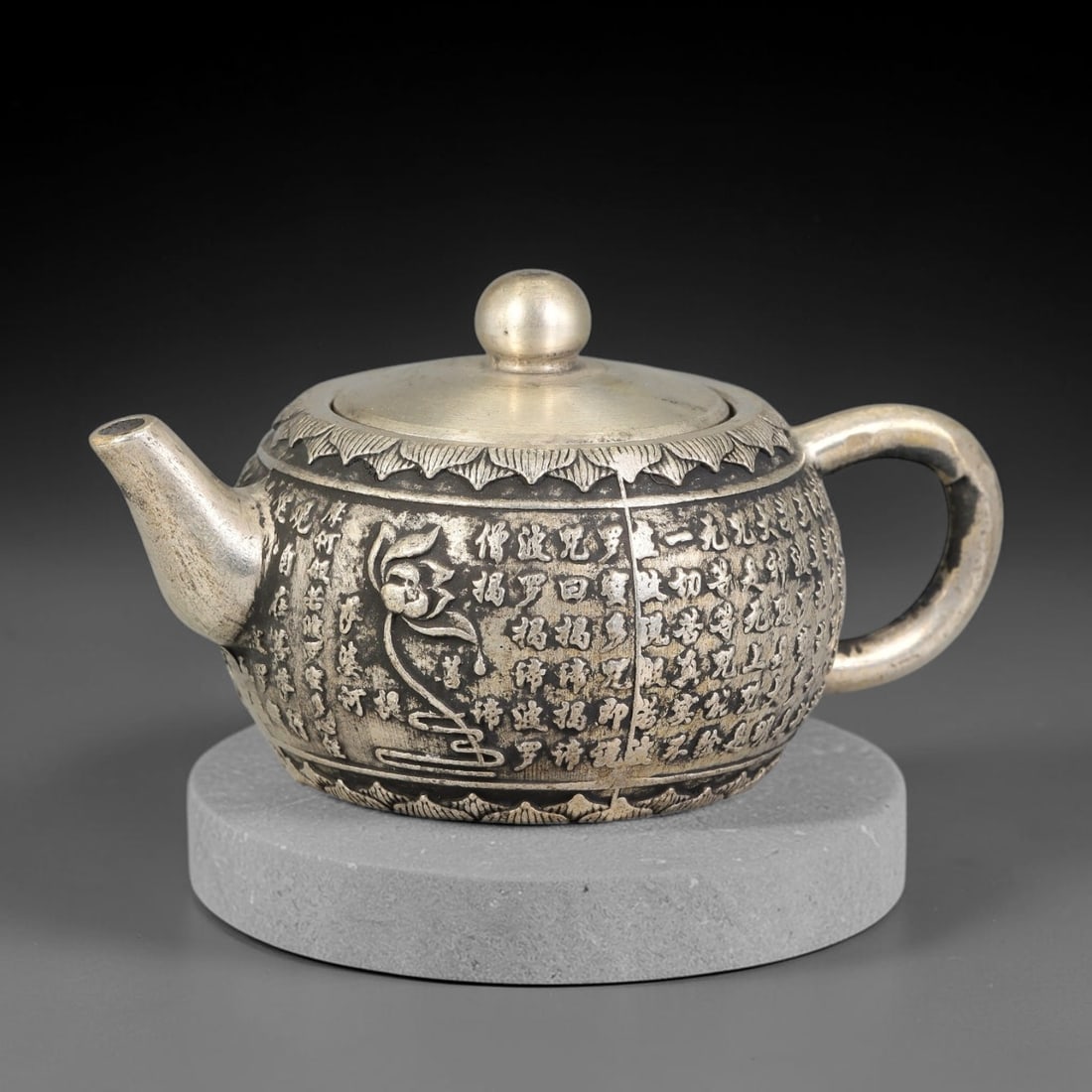 A Chinese German Silver Heart Sutra Teapot, 53BD: Cast German silver teapot with a rounded body decorated in relief with the full text of the Heart Sutra alongside a lotus bloom motif. Stylised lotus petal borders run along the rim and base, fitted w
