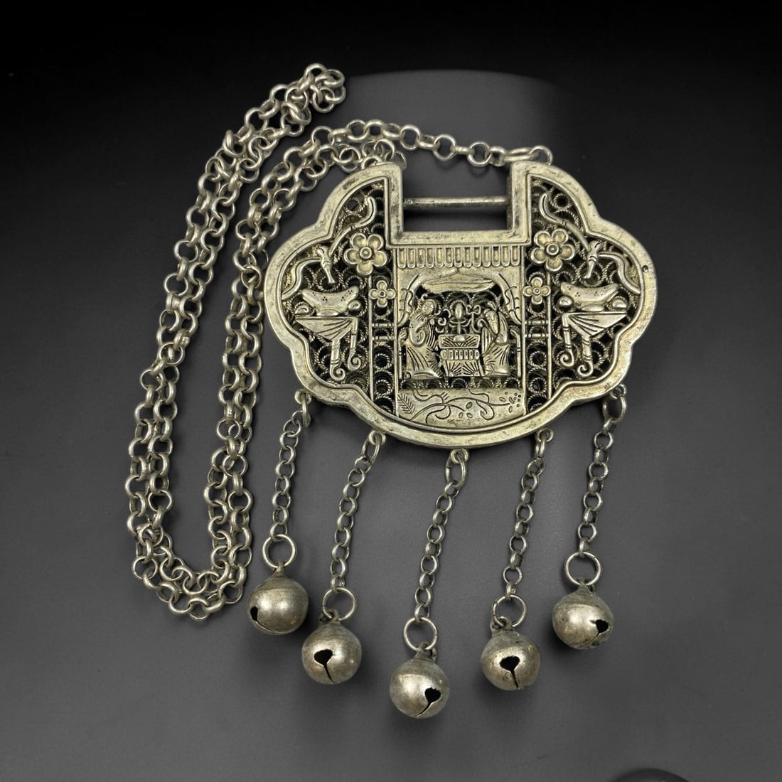 A Chinese Filigree German Silver Hundred Family Lock Pendant Necklace, 93BD: Filigree constructed German silver ruyi-form lock pendant, the obverse finely worked with a figural scene within a pavilion surrounded by floral and avian ornament. The reverse bears the inscribed cha