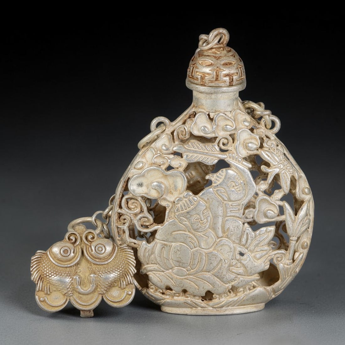 A Chinese German Silver Openwork Snuff Bottle with Children and Lotus Motif, 14AV: Pear-shaped German silver snuff bottle with intricate reticulated openwork carving. The pierced exterior depicts children upon lotus blooms, accented by cloud scrolls, bamboo and insect details. The s