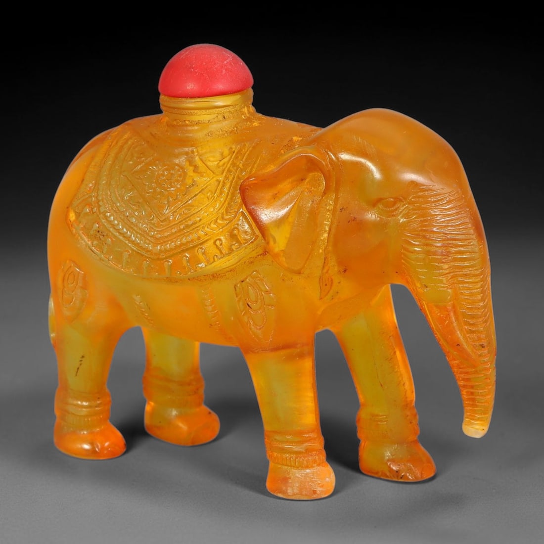 A Chinese Amber Resin Elephant Form Snuff Bottle, 49AV: Figural snuff bottle fully modelled in the form of an elephant from translucent amber resin, with finely carved decorative saddle cloth and body ornamentation, detailed ears, trunk and leg anklets. Th