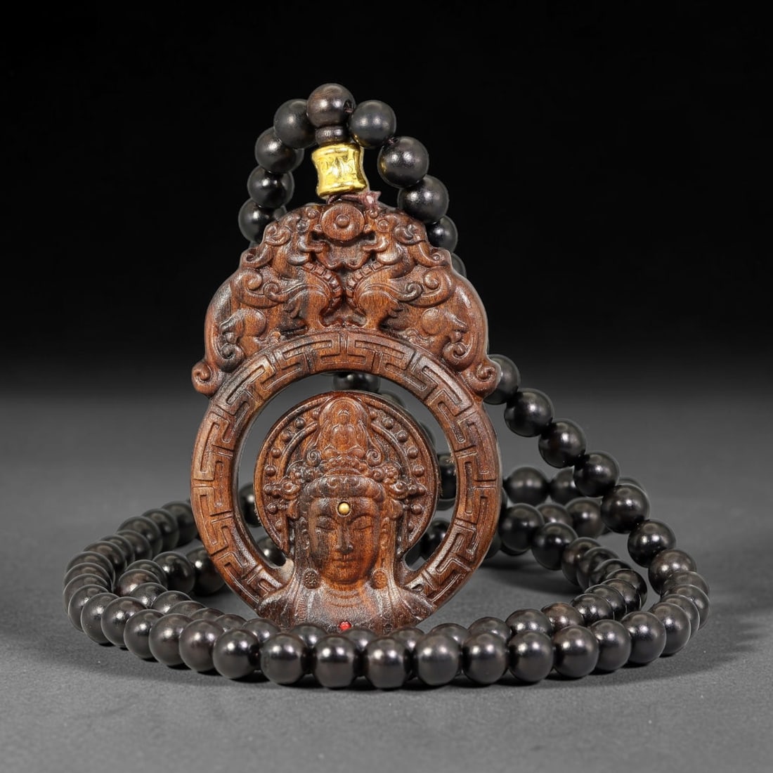 A Chinese Carved Wood Rotatable Guanyin Pendant with Beaded Necklace, 82BD: Openwork carved wood pendant with a rotating central Guanyin medallion inset with a tiny golden dot detail. The upper section is relief carved with paired mythical beasts above geometric key-fret bord