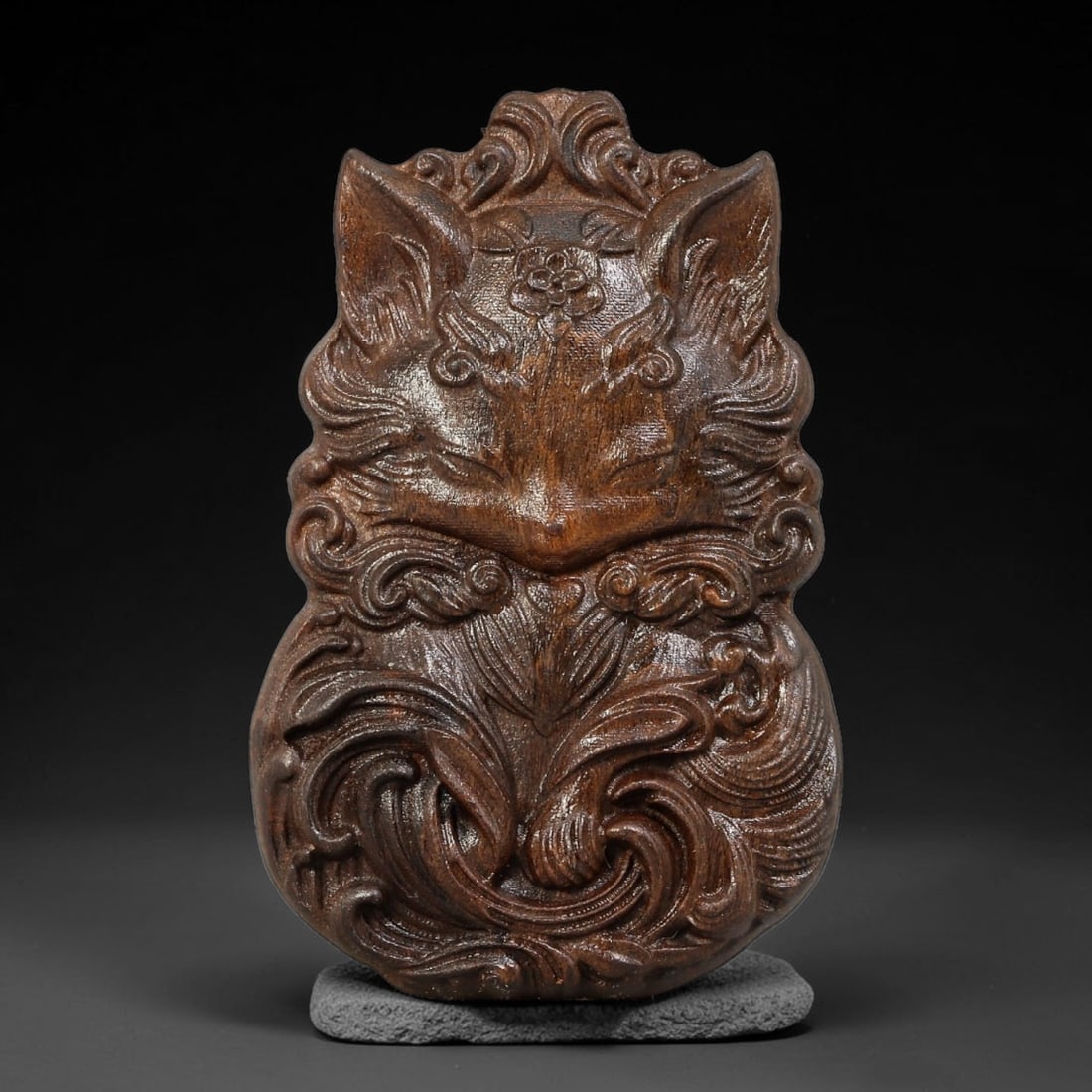 A Chinese Carved Wood Nine-Tailed Fox Pendant, 5BF: Relief carved wood pendant depicting a nine-tailed fox motif with curled ornamental scrollwork framing the face and flowing tails. Fine carved floral detail sits on the forehead, with decorative scrol