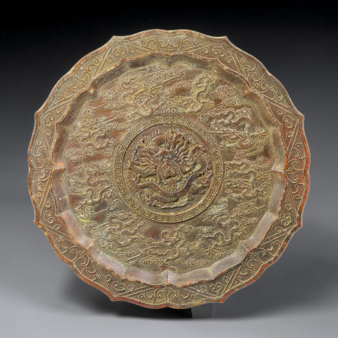 A Chinese Bronze Nine Dragon Lobed Dish, 45BD: Cast bronze dish with a multi-lobed scalloped rim. The interior is decorated in relief with a central dragon roundel enclosed within a key-fret border. The surrounding field bears further dragon figur