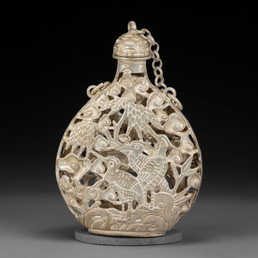 A Chinese German Silver Openwork Snuff Bottle with Cranes and Qilin, 16AV: Pear-shaped German silver snuff bottle with intricate reticulated openwork carving. The pierced body is decorated with cranes and qilin amidst swirling cloud scrolls, rocks and bamboo. The stopper fea