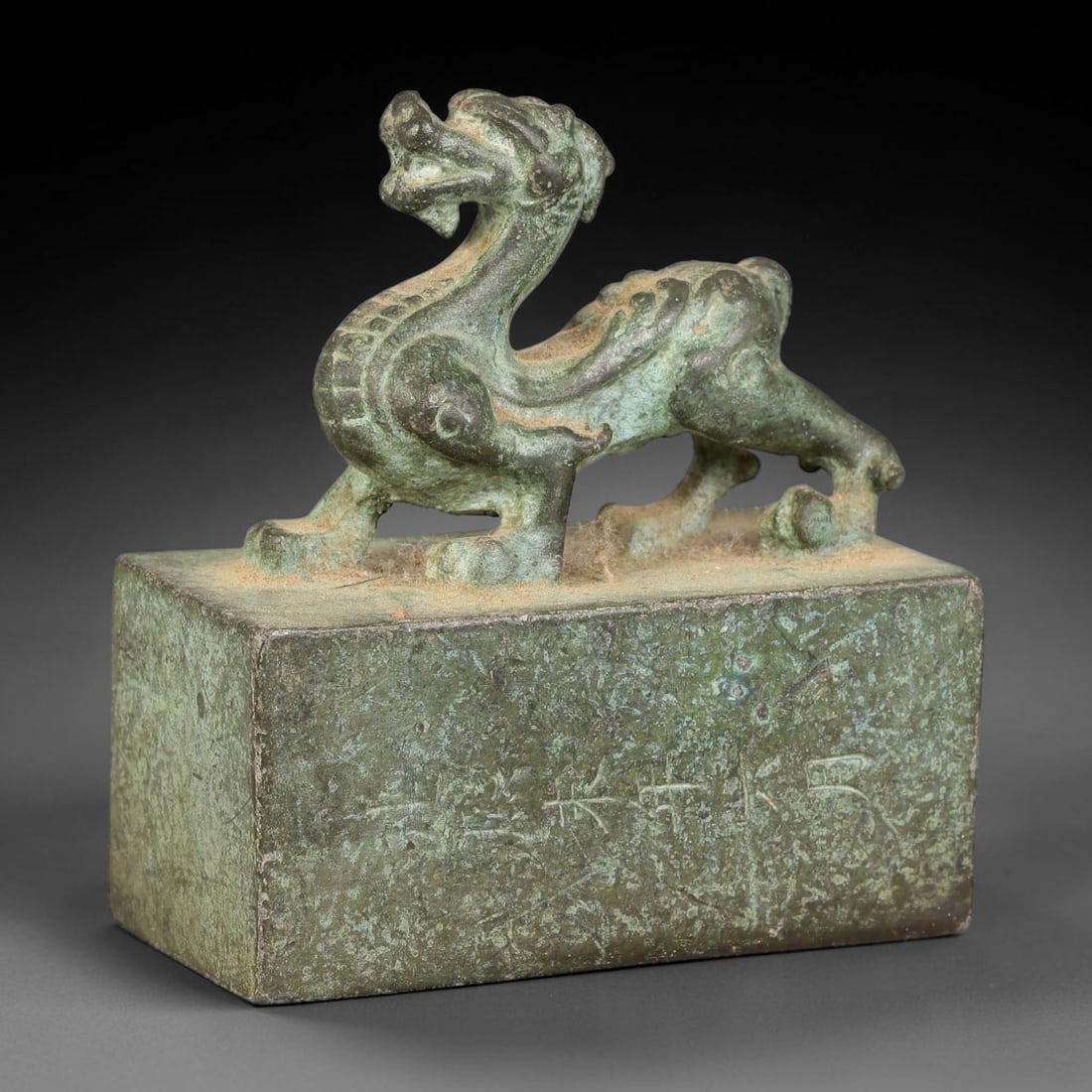 A Chinese Bronze Mythical Beast Seal, 82AX: Cast bronze rectangular seal surmounted by a prowling mythical beast finial with raised relief detailing along its spine and limbs. The vertical side bears an engraved inscription, while the seal face
