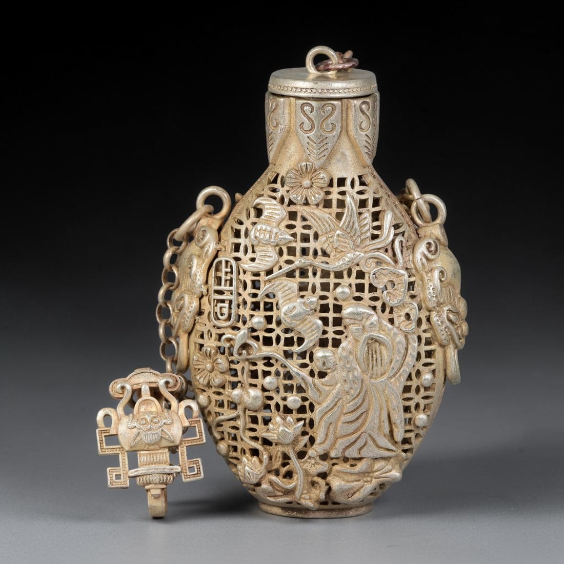 A Chinese German Silver Openwork Snuff Bottle with Figural and Bat Motifs, 24AV: Ovoid German silver snuff bottle with fine reticulated openwork carving, decorated with a robed figure, flying bats, blossoms and auspicious emblems set upon lattice ground. The neck bears repeating s