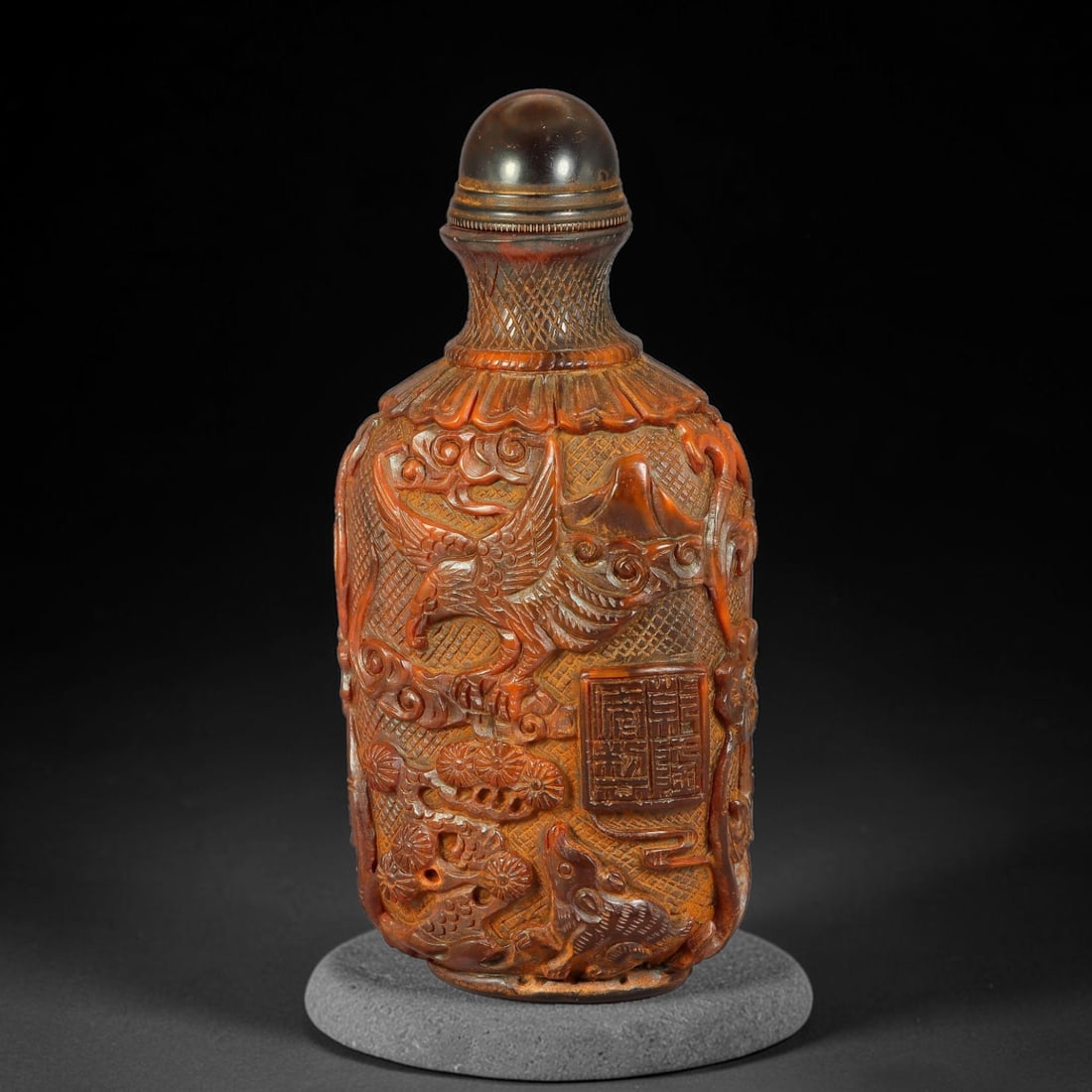 A Chinese Amber Resin Deep Relief Carved Snuff Bottle, 69AV: Tall rectangular snuff bottle crafted from amber resin, intricately carved in deep relief on both sides with phoenix, pine trees, cloud scrolls and seal mark panels over a fine diaperwork background. 