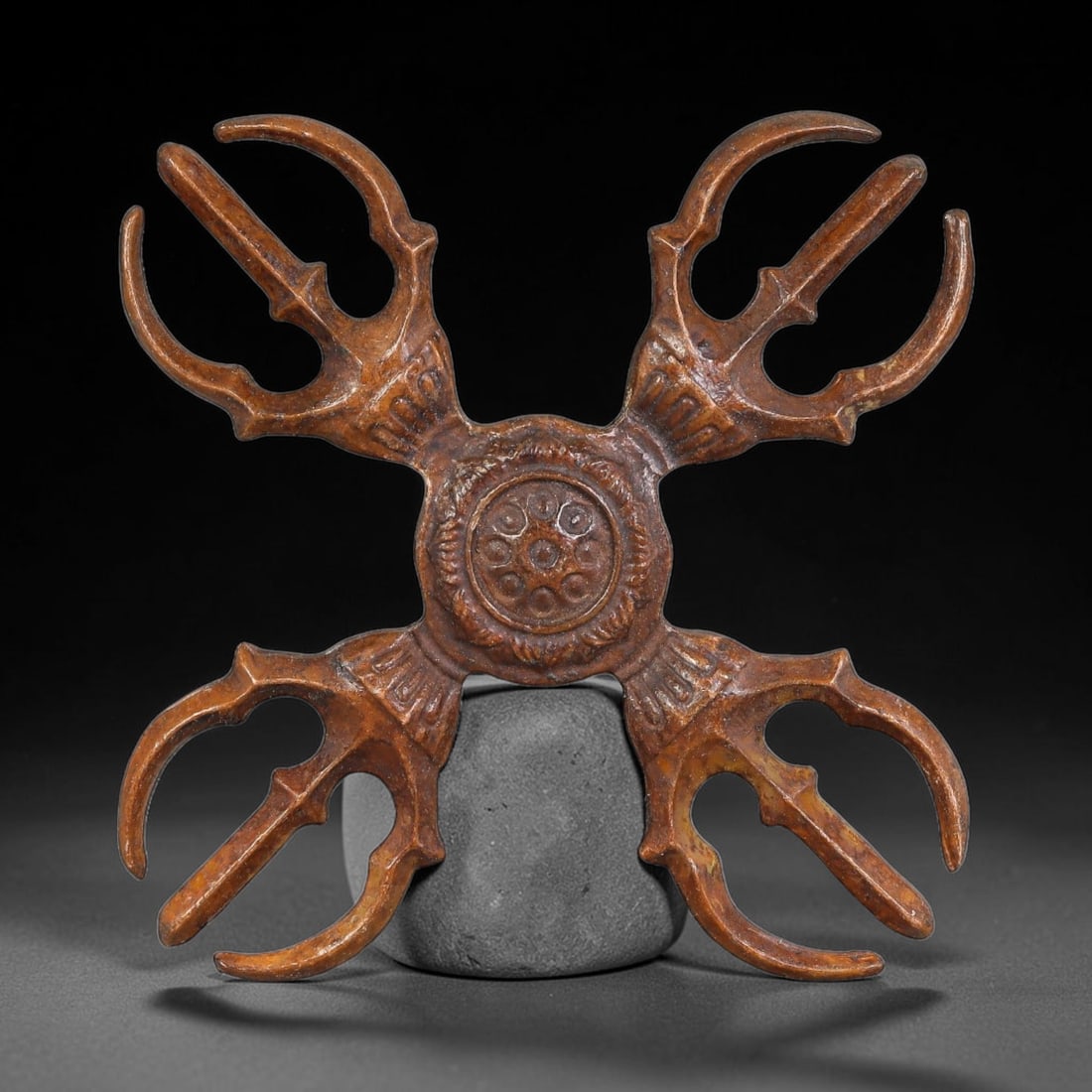 A Chinese Bronze Four-Pointed Vajra Ritual Implement, 55AD: Cast bronze ritual four-pointed vajra, four symmetrical trident-style prongs radiating outward from an ornate central circular boss decorated with rosette and foliate relief motifs. Mellow warm brown 