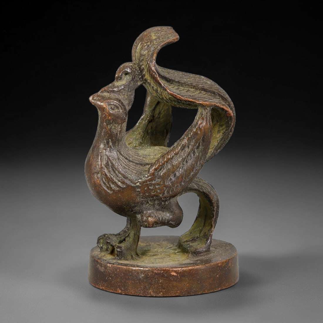 A Chinese Bronze Phoenix Finial Seal, 79BT: Cast in bronze, the seal features a standing phoenix handle with elegantly curved feathered wings, incised plumage detailing and defined facial features, mounted upon a solid circular base. The flat b