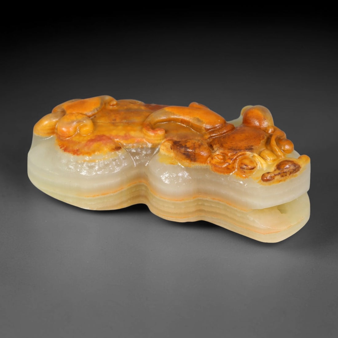 A Chinese Banded Calcite Carved Pixiu Pendant, 31BX: This pendant is carved from banded calcite, displaying distinct stratified layers of creamy pale white base with warm orange-brown natural skin tones across the upper surface. Relief carving forms a r