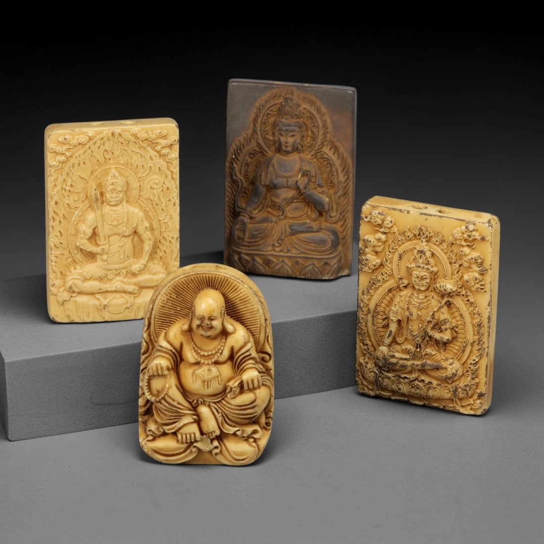A Group of Four Chinese Creamy Beige Tagua Nut Carved Religious Figure Pendants, 73CB: This finely carved group of four pendants is made of tagua nut with a warm creamy beige tone, comprising two rectangular relief plaques carved with seated bodhisattva figures, one rectangular relief p