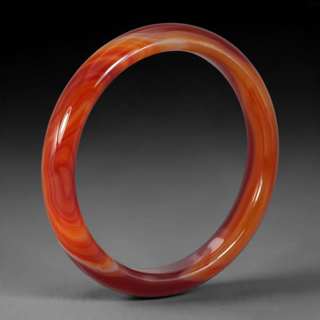 A Chinese Sardonyx Banded Agate Bangle Bracelet, 4AE: This polished round bangle is carved from natural sardonyx, exhibiting a deep saturated carnelian red hue with a fine thin pale band inclusion across the smooth, high-gloss surface. It features consis