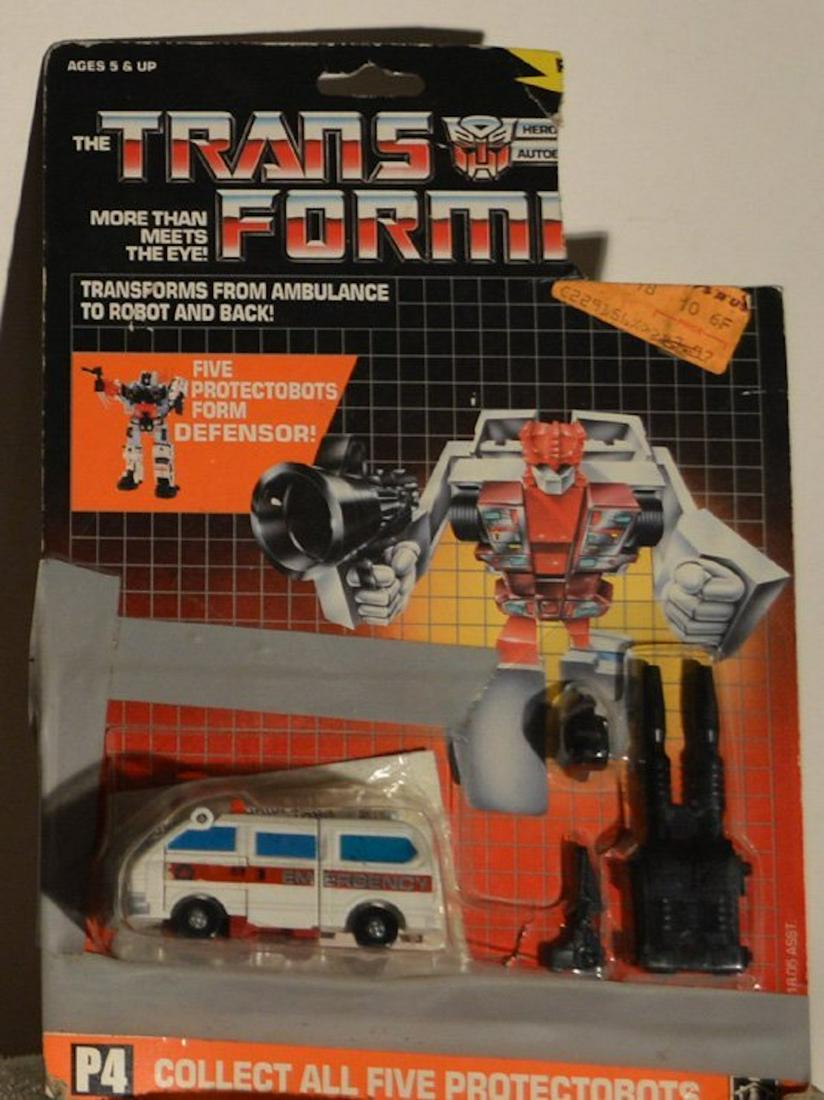THE TRANSFORMERS "FIRST AID": THE TRANSFORMERS "FIRST AID".TRANSFORMS FROM AMBULANCE TO ROBOT AND BACK.FIVE PROTECTORBOTS FORM DEFENSOR!.THIS ITEM WAS TAPED TO THE ORIGINAL PACKAGING (SEE PICTURES).COMPLETE AND INTACT