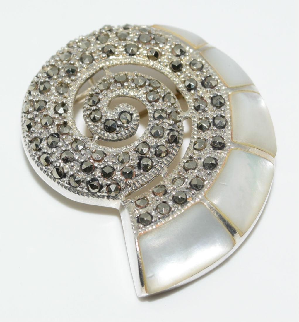 Sterling Silver Nautilus Pendant/Brooch: Sterling silver nautilus pendant and brooch. This beautiful piece is set with a swirl of marcasite and mother of pearl. | Measurement: 1 ¼” | Weight: 9 grams | Stamp: 925 CFJ Thai
