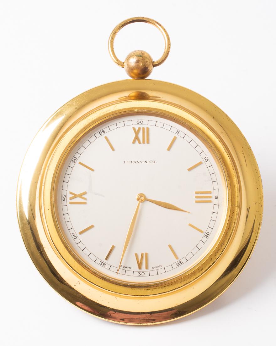 Tiffany & Co 8-Day Travel Clock 5.75" Diameter: Description: Vintage Tiffany & Co 8-Day Swiss made travel clock. Resembles an over-sized pocket watch, ball-footed on back, lays flat on table. Brass case, hands and Roman numerals, gray