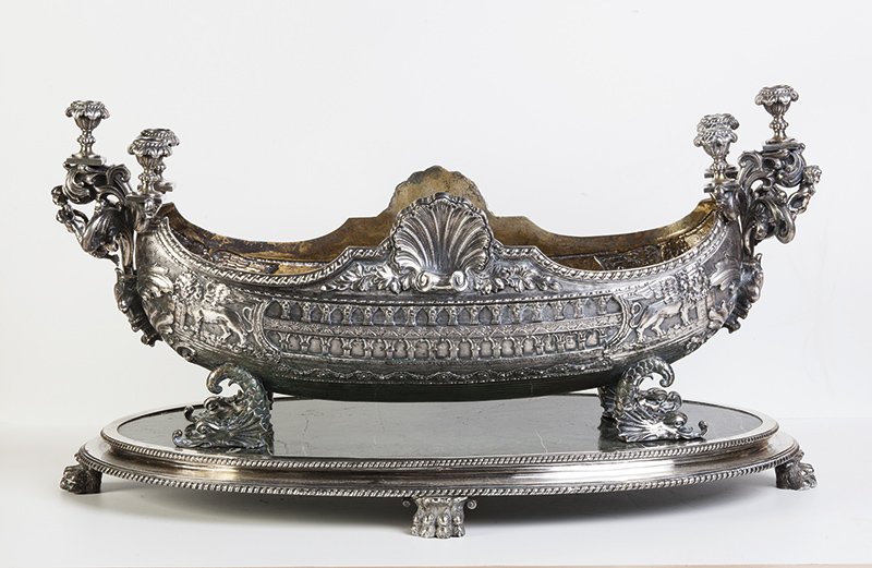 Bucintoro in argento titolo 800: in stile barocco, manifattura dei primi anni del Novecento; il vaso presenta decori a rilievo con motivi tipichi dell’iconografia veneziana, quale i leoni alati di San Marco; due conciglie sul bordo