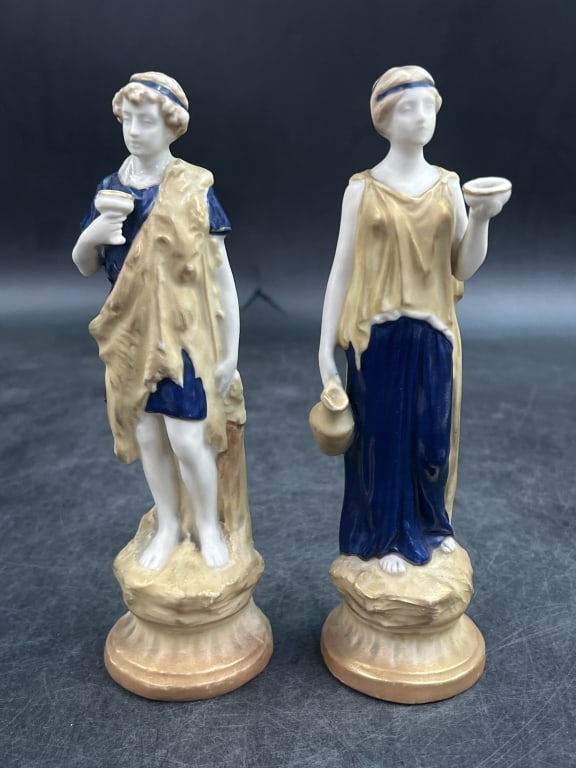 Antique Royal Dux Porcelain Figurines: Depicts a pair of water carriers carrying amphora vases. Produced in Bohemia now known as Czech Republic. Figures feather polychrome accents in shades of taupe, pink and amber. Marked pink triangle wi