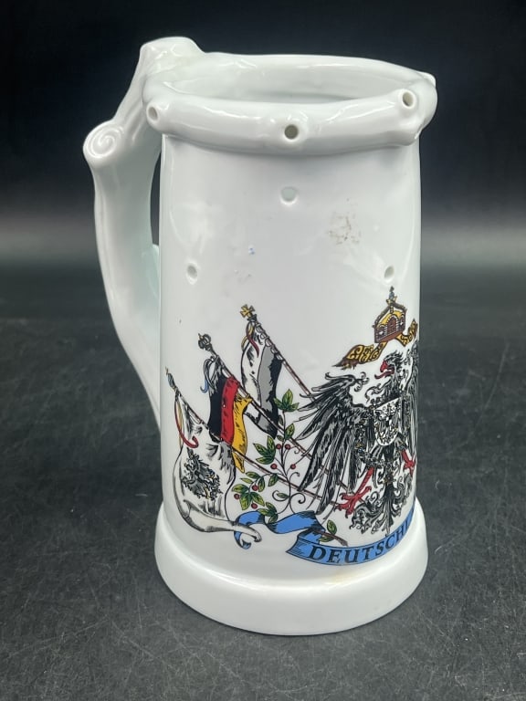 Puzzle Stein or Trick Stein: Deutschland Eagle Mug, with nude litho, often featuring white porcelain body with German Flag and eagle motifs. Mug has holes around top rim, designed to make it difficult to drink from without