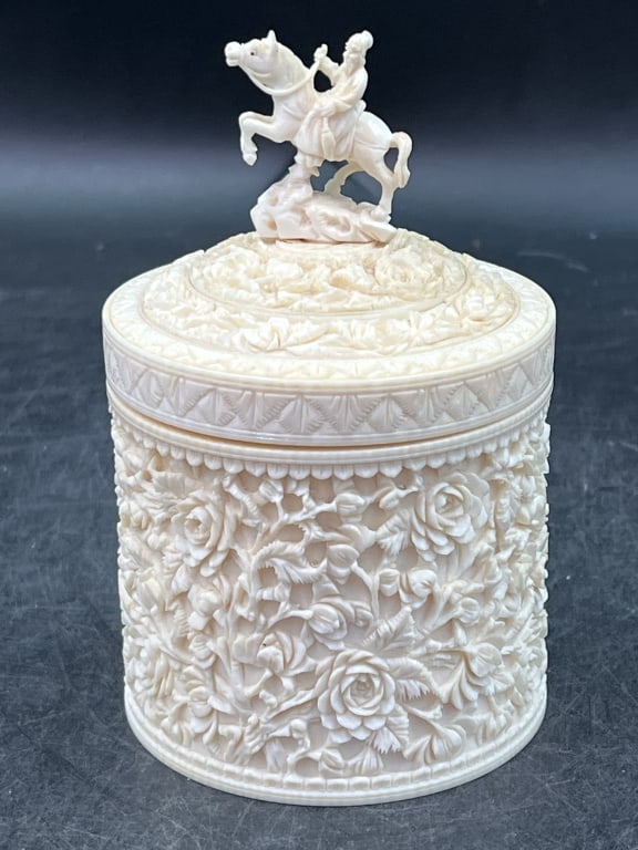 Vintage Composite/Trinket Box: Featuring intricate floral relief on the body and a finial on the lid depicting figure on horseback. Round lidded box with high relief rose floral patterns. Measures 5" x 3 1/4". Condition is