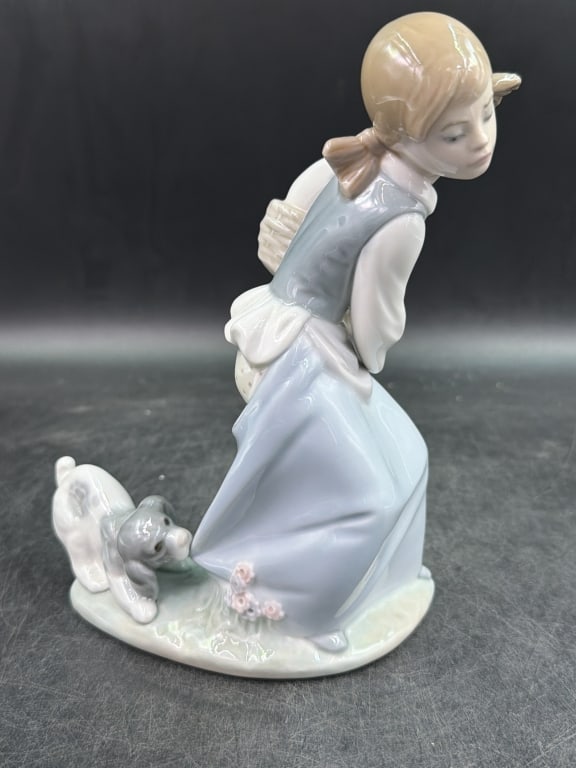 Lladro 'Naughty Dog': Depicts a young girl carrying a basket while playful pupps tugs tightyl on the back of her skirt. Measures 8" and condition is good, see pictures. No refunds given.