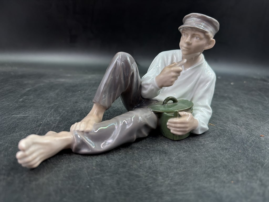 Vintage Royal Copenhagen 'Shepherd Boy at Lunch': Young boy or fisherman wearing a cap, reclining comfortably barefoot on the ground while eating out of a lunchbox. Marked on the bottom. Measures 4 x 7.5". Condition is good, see pictures. No refunds