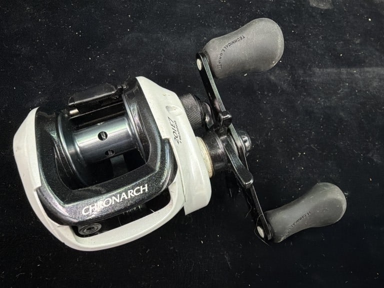 Shiman Chronarch E Series 201E7 Baitcasting Reel: Left hand retired. distinct white frame ported metallic spool and Chronarch branding. Condition is used, see pictures (appears good). No refunds given.