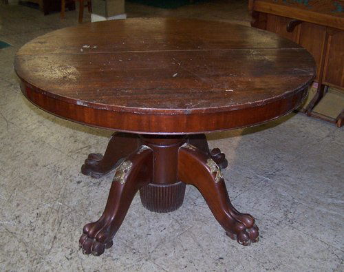 MAHOGANY ROUND CLAWFOOT DINING TABLE: A 19TH CENTURY CLAWFOOT DINING TABLE WITH BRASS LION APPLIQUES. ITEM HAS ROUGH FINISH DUE TO WEATHERING. NO DAMAGE TO WOOD, JUST A FINISH ISSUE.