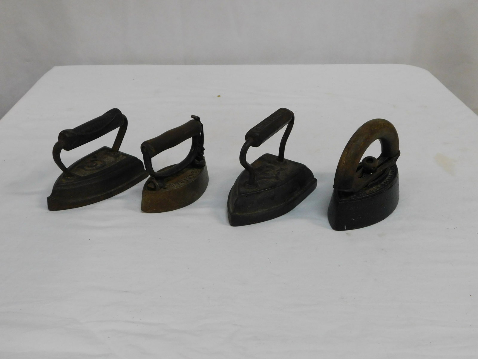 4 Cast Iron Sad Irons: 4 Cast Iron Sad Irons in good condition. #7 marked Geneva, IL., #6 marked with a C, Large wooden handle one is marked Enterprise Manufacturing Co. Philadelphia, and small wooden handle is marked Sensi