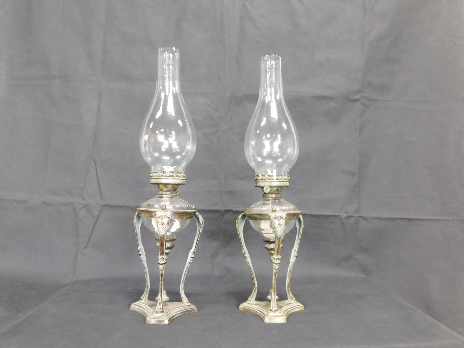 Pair of Vintage Metal Oil Lamps w/Bronze Wash: Pair of Vintage Metal Oil Lamps with a Bronze Wash. Glass Fonts Set in a Metal Stand with Cast Faces on Each of Three Legs. Blown Glass Chimneys. Functional but Appear to Have Ever Been Used. 24"H in 