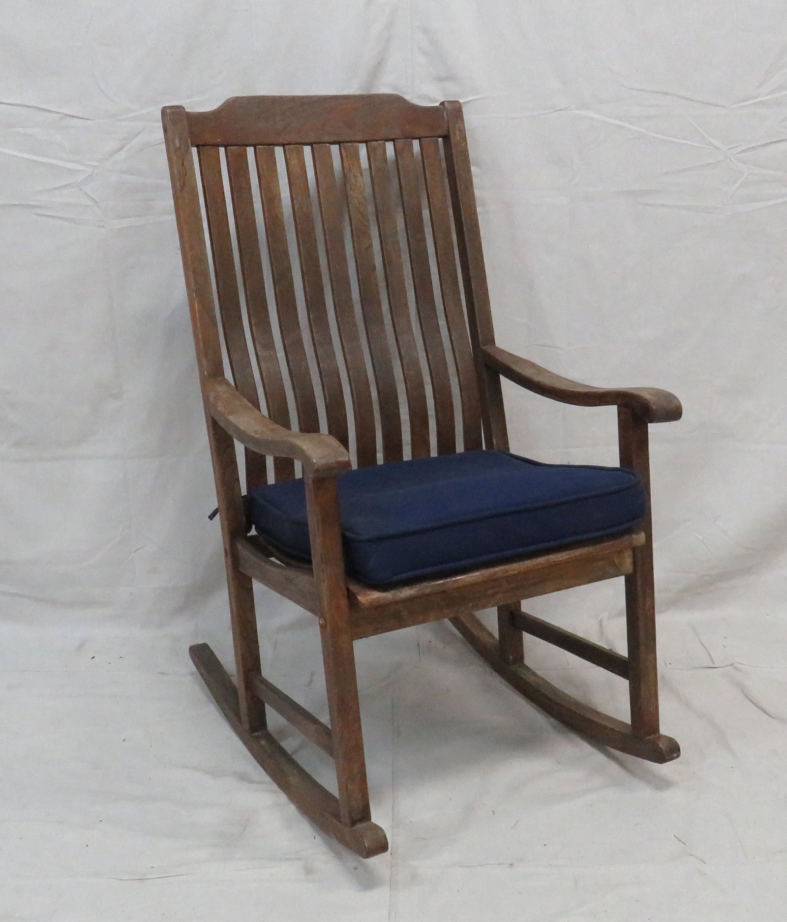 Large Teakwood Rocking Chair: Large Teakwood Rocking Chair. Structurally sound with weathered finish. Cushion in good condition. 45"H x 25"W x 32"D