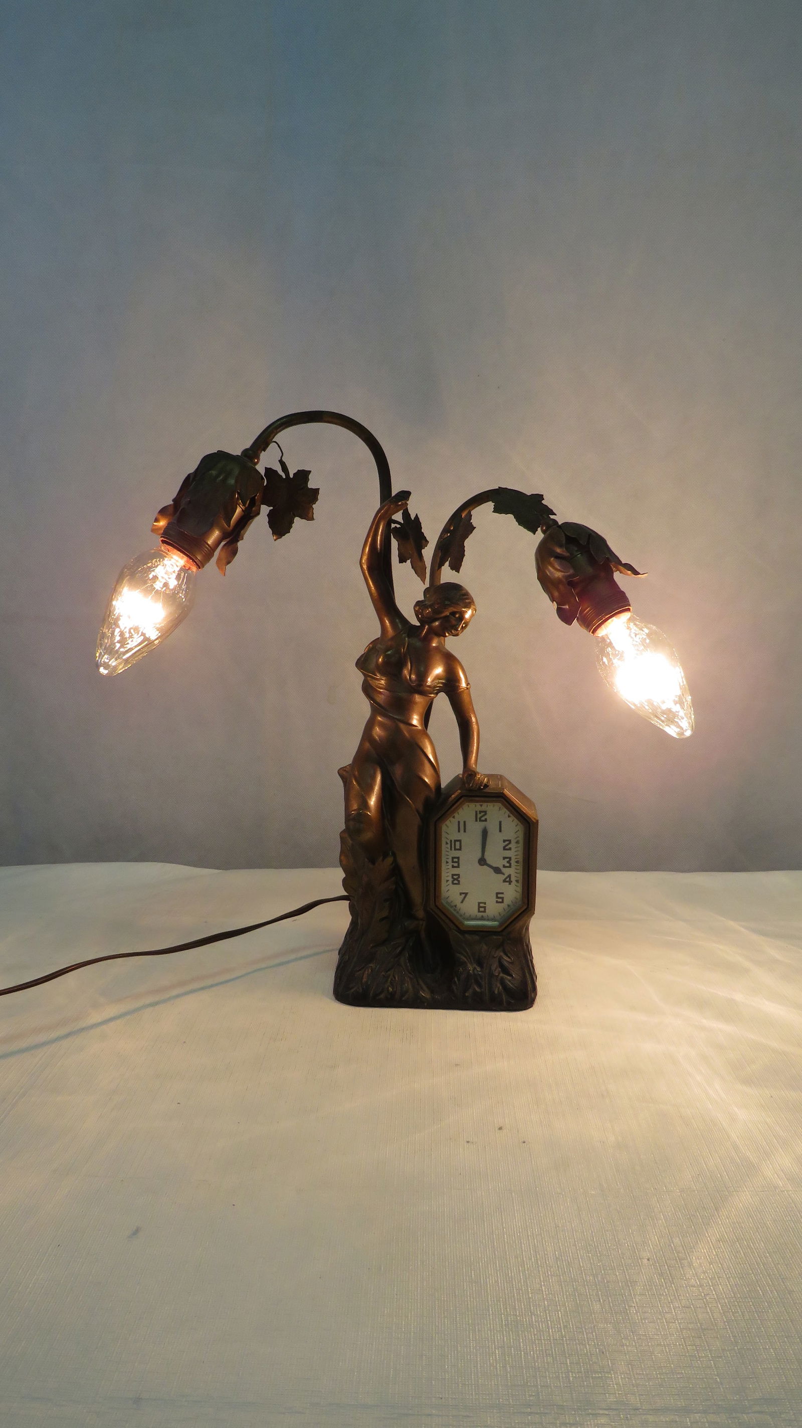 1920s Art Nouveau Figural Lamp with Clock: 1920s Art Nouveau Figural Lamp with Clock in good condition. Clock is not currently working. Metal figural lamp with bronze wash. Clock was made by Schadow & Sons in New York, NY. 15"H