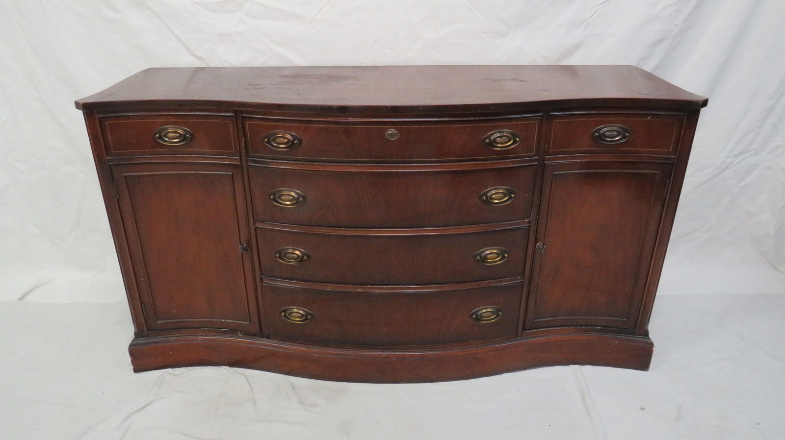 Traditional Mahogany Serpentine Bassett Sideboard: Traditional Mahogany Serpentine Bassett Sideboard in as found condition, Top has finish issues, otherwise in good condition, String Inlaid, Dovetailed Drawers with Brass Hardware, 33''H x 63''W x 22''